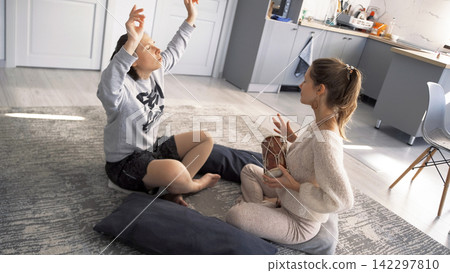 Two roommates threw a party with drum rhythms. Trance and music. The women are sitting on the floor, one of them is playing a drum Two roommates threw a party with drum rhythms. Trance and music. The women are sitting on the floor, one of them is playing a drum 142297810
