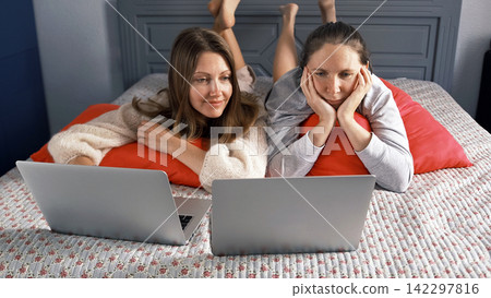 The roommates are lying on the bed and watching movies on their laptop. Two lesbians having fun in the bedroom The roommates are lying on the bed and watching movies on their laptop. Two lesbians having fun in the bedroom 142297816