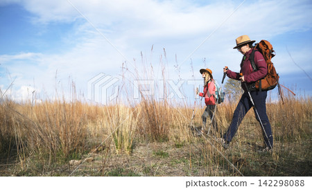 A tour guide and a tour instructor are exploring new routes for commercial hikes. Two women are walking through a field 142298088
