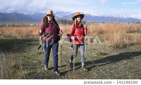 The spirit of adventurism and adventure. Two pretty young students are strolling through a grassy field against the backdrop of snow-capped mountains The spirit of adventurism and adventure. Two pretty young students are strolling through a grassy field against the backdrop of snow-capped mountains 142298100