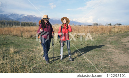 Two travelers enjoy a walk in the fresh air at sunset in a field near the snow-capped mountains. A lesbian couple is hiking. Active weekends Two travelers enjoy a walk in the fresh air at sunset in a field near the snow-capped mountains. A lesbian couple is hiking. Active weekends 142298101