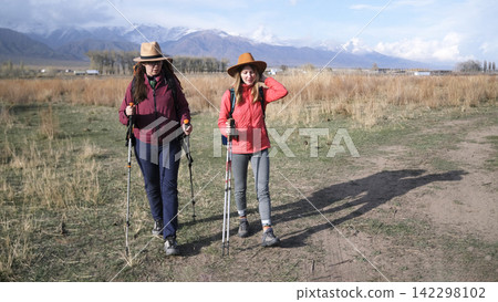 Two lesbians in hats are walking in the countryside. The women gathered for a picnic. Female students with backpacks and trekking poles Two lesbians in hats are walking in the countryside. The women gathered for a picnic. Female students with backpacks and trekking poles 142298102