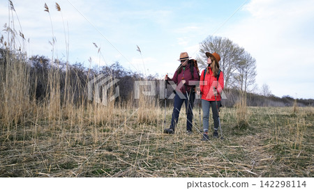 Two women are wandering through a field overgrown with tall grass. Travel and adventures. Weekend camping trip. A walk in the fresh air Two women are wandering through a field overgrown with tall grass. Travel and adventures. Weekend camping trip. A walk in the fresh air 142298114