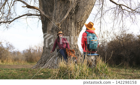 Two young beautiful lesbians are chatting sweetly and naturally with each other sitting under a big old tree. Hikers are resting 142298158