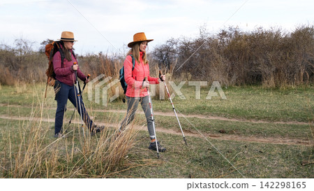 A lesbian family is heading to the holy places. Two women are walking through a field with backpacks and trekking poles A lesbian family is heading to the holy places. Two women are walking through a field with backpacks and trekking poles 142298165