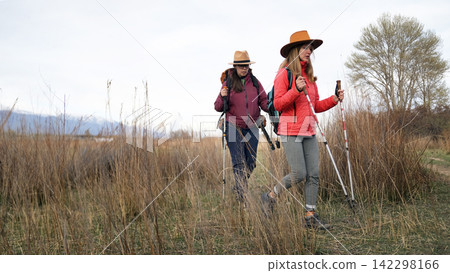 Two female tourists are walking through a field overgrown with tall yellow grass. Journey, expedition and freedom. The spirit of adventurism 142298166