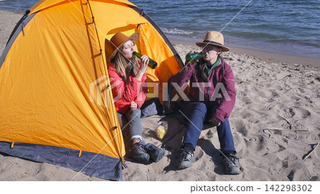 The problem of female alcoholism. Two people are sitting in a tent on the beach and drinking beer. Lesbians on a romantic date by the lake The problem of female alcoholism. Two people are sitting in a tent on the beach and drinking beer. Lesbians on a romantic date by the lake 142298302