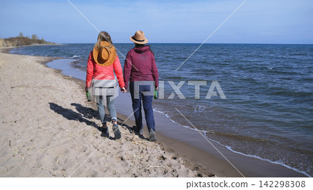 Two women are strolling along the beach against the background of the blue ocean. Tourists wander along the seashore with beer bottles Two women are strolling along the beach against the background of the blue ocean. Tourists wander along the seashore with beer bottles 142298308