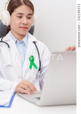 doctor using laptop for telehealth, online consultation and meeting about green ribbon for July Eye Injury Prevention month, February Gallbladder and Bile duct and October Liver cancer Awareness month 142298351