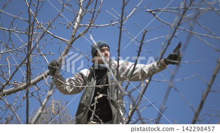 Professional tree pruner. A handsome white guy is pruning dry branches in the garden. A man cuts branches from a tree Professional tree pruner. A handsome white guy is pruning dry branches in the garden. A man cuts branches from a tree 142298457