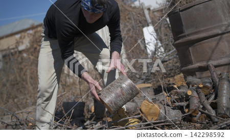 A man holds a log in his hands. Harvesting of firewood. The log is lying in a pile of firewood. The man is wearing a black shirt and beige work trousers A man holds a log in his hands. Harvesting of firewood. The log is lying in a pile of firewood. The man is wearing a black shirt and beige work trousers 142298592