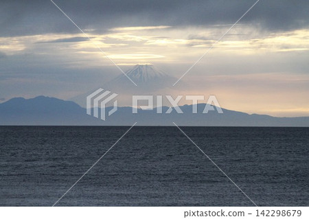 Mount Fuji at sunset, with sunlight shining through a break in the clouds, as seen from Tateyama-Hojo Beach. Mount Fuji at sunset, with sunlight shining through a break in the clouds, as seen from Tateyama-Hojo Beach. 142298679
