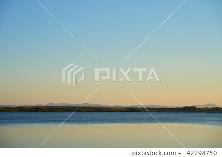 Calm lake with distant mountains under clear blue sky Calm lake with distant mountains under clear blue sky 142298750