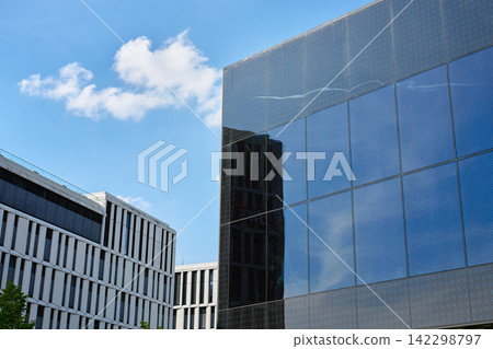 Modern reflective glass building under blue sky with clouds Modern reflective glass building under blue sky with clouds 142298797