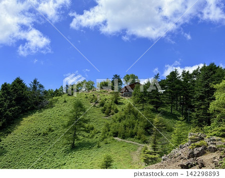 從東京最高峰雲取山頂眺望富士山和夏季山景,周圍環繞著藍天和積雲,以及雲取山避難小屋。 從東京最高峰雲取山頂眺望富士山和夏季山景,周圍環繞著藍天和積雲,以及雲取山避難小屋。 142298893