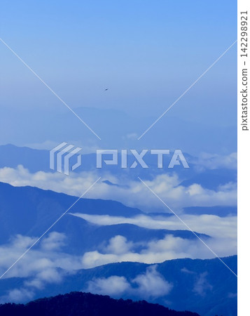 從東京最高峰雲取山頂眺望富士山和夏季山景,周圍環繞著藍天和積雲,以及雲取山避難小屋。 從東京最高峰雲取山頂眺望富士山和夏季山景,周圍環繞著藍天和積雲,以及雲取山避難小屋。 142298921