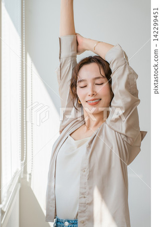 A beautiful female model stretching by the living room window. A beautiful female model stretching by the living room window. 142299451