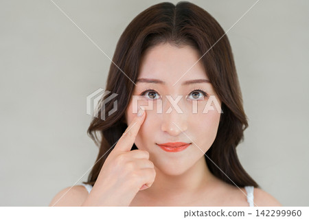 一張四、五十歲女性的美麗照片，她指著自己的眼睛和臉頰，仔細端詳。 142299960
