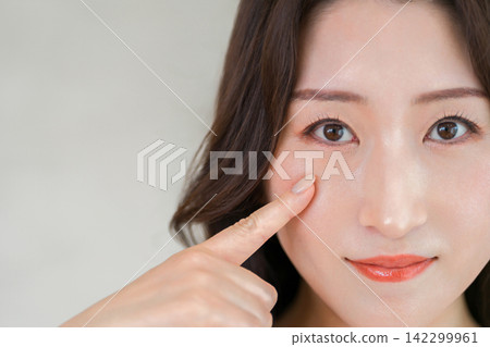 一張四、五十歲女性的美麗照片，她指著自己的眼睛和臉頰，仔細端詳。 142299961