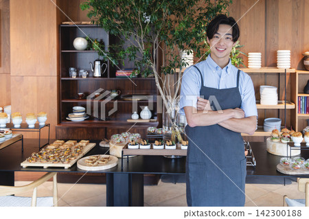 一位咖啡館裡的男士微笑地站在那裡，背景是自助餐食物。 142300188
