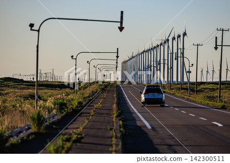 一輛 SUV 沿著筆直的道路飛馳,遠處是北海道幌延町大頓瑞風力發電廠的風力渦輪機。 一輛 SUV 沿著筆直的道路飛馳,遠處是北海道幌延町大頓瑞風力發電廠的風力渦輪機。 142300511