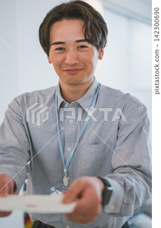 辦公室戀情場景:一位二十多歲的商人面帶微笑,遞上一個信封。 辦公室戀情場景:一位二十多歲的商人面帶微笑,遞上一個信封。 142300690