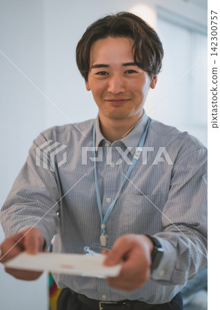 辦公室戀情場景:一位二十多歲、微笑的商務男士,手裡拿著一個信封。 辦公室戀情場景:一位二十多歲、微笑的商務男士,手裡拿著一個信封。 142300757