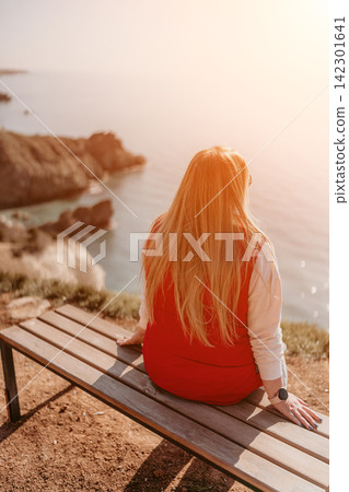Woman coast sunset sitting on a wooden bench overlooking the scenic rocky cliffs and sea during a golden hour Woman coast sunset sitting on a wooden bench overlooking the scenic rocky cliffs and sea during a golden hour 142301641