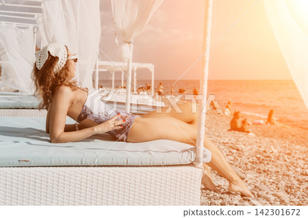 Woman beach vacation relaxed lady lying on a white cabana bed at a stony shore during sunset with sea background 142301672
