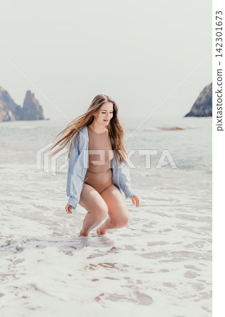 Woman beach ocean young female with long hair playing in waves wearing a bodysuit and blue shirt on a summer day 142301673
