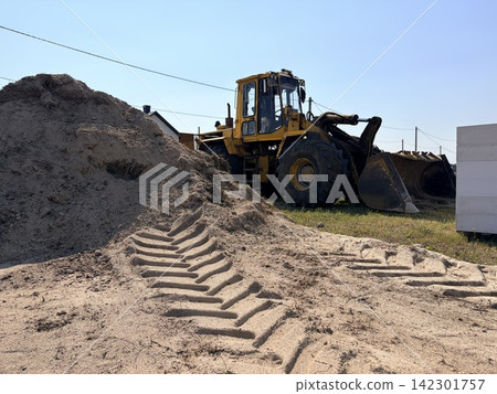 A yellow wheel loader is parked next to a sand embankment at a construction site. Heavy equipment, construction work A yellow wheel loader is parked next to a sand embankment at a construction site. Heavy equipment, construction work 142301757