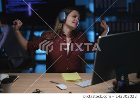Businesswoman stretches arms while wearing headphones at office Businesswoman stretches arms while wearing headphones at office 142302028
