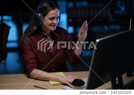 Businesswoman waves at monitor during remote office meeting Businesswoman waves at monitor during remote office meeting 142302029