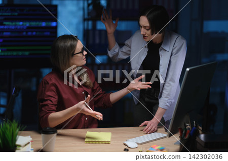 Businesswomen argue during tense late office discussion at table Businesswomen argue during tense late office discussion at table 142302036