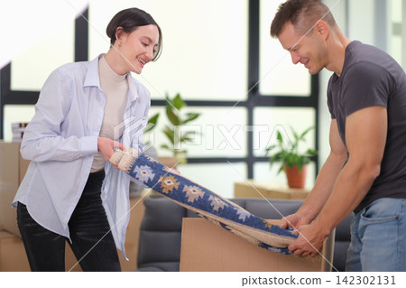 Happy married couple takes carpet out of box in new apartment Happy married couple takes carpet out of box in new apartment 142302131