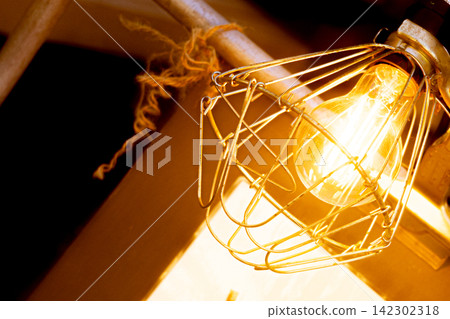 An Edison light bulb glows warmly inside a metal cage. An Edison light bulb glows warmly inside a metal cage. 142302318
