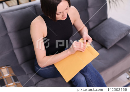Curious woman opens paper envelope containing personal letter Curious woman opens paper envelope containing personal letter 142302566