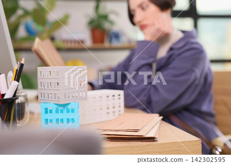 Woman works near miniature building models at office desk 142302595