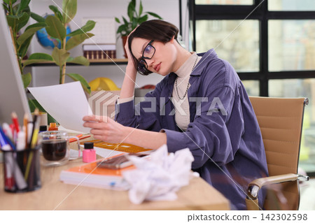 Worried woman reviews document while sitting at office desk Worried woman reviews document while sitting at office desk 142302598