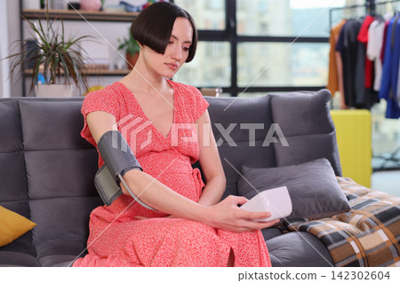 Pregnant woman checks blood pressure with digital monitor at home Pregnant woman checks blood pressure with digital monitor at home 142302604