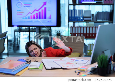 Scared woman employee hides behind desk from emails on computer Scared woman employee hides behind desk from emails on computer 142302860