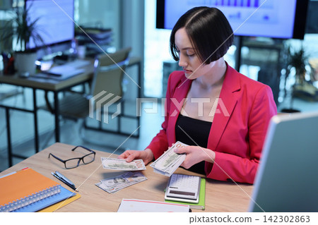 Young businesswoman counts cash money over desk in office Young businesswoman counts cash money over desk in office 142302863
