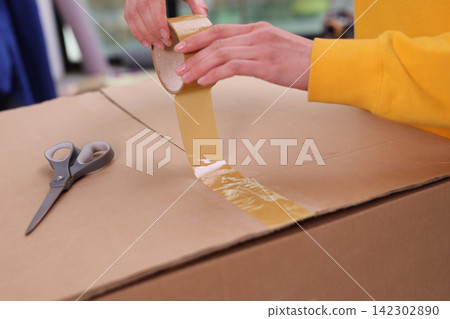 Woman hands pack cardboard box with adhesive tape at home Woman hands pack cardboard box with adhesive tape at home 142302890