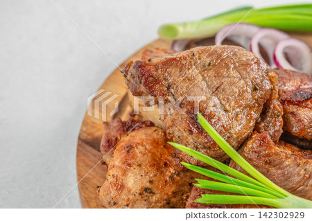 Grilled meat pieces arranged on a wooden platter with green onions and red onion slices, showcasing a delicious and appetizing presentation of cooked food Grilled meat pieces arranged on a wooden platter with green onions and red onion slices, showcasing a delicious and appetizing presentation of cooked food 142302929
