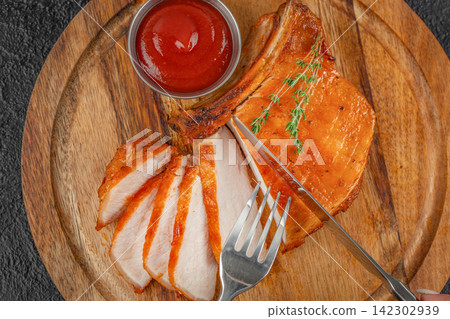 Grilled pork chops arranged on a wooden plate alongside a bowl of ketchup and fresh green onions on a light textured surface Grilled pork chops arranged on a wooden plate alongside a bowl of ketchup and fresh green onions on a light textured surface 142302939