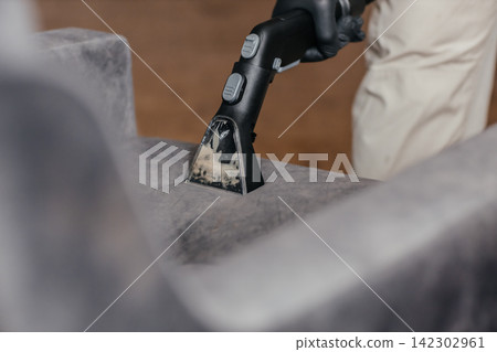 Professional upholstery extraction cleaning on gray fabric armchair with vacuum cleaner nozzle Professional upholstery extraction cleaning on gray fabric armchair with vacuum cleaner nozzle 142302961