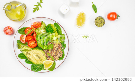 Fresh vegetable salad with quinoa, cherry tomatoes, avocado, and broccoli on a white plate, surrounded by olive oil, lemon, and pumpkin seeds on a clean surface Fresh vegetable salad with quinoa, cherry tomatoes, avocado, and broccoli on a white plate, surrounded by olive oil, lemon, and pumpkin seeds on a clean surface 142302993