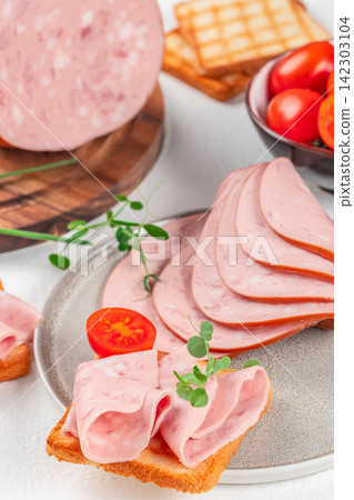 Slices of pink luncheon meat arranged on a plate with cherry tomatoes and crackers, garnished with fresh herbs on a white background Slices of pink luncheon meat arranged on a plate with cherry tomatoes and crackers, garnished with fresh herbs on a white background 142303104