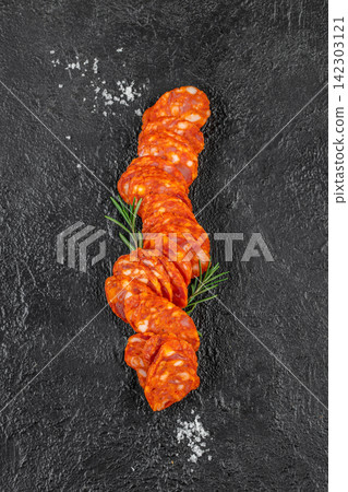 Sliced chorizo sausage arranged on a dark textured surface with fresh rosemary and coarse sea salt sprinkled around for a gourmet food presentation Sliced chorizo sausage arranged on a dark textured surface with fresh rosemary and coarse sea salt sprinkled around for a gourmet food presentation 142303121