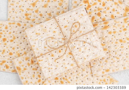 Flatbreads arranged in a circular pattern with a tied bundle of matzo in the center, showcasing a textured surface and light brown speckles on a white background Flatbreads arranged in a circular pattern with a tied bundle of matzo in the center, showcasing a textured surface and light brown speckles on a white background 142303389